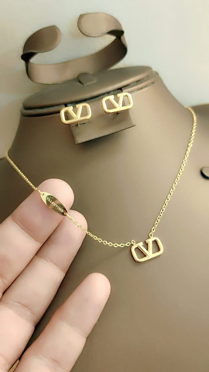 Gold necklace and earrings on a mannequin with a hand holding the necklace.