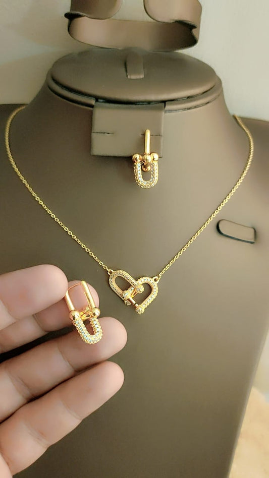 Gold heart-shaped necklace and earrings on a mannequin bust with a hand holding additional earrings.
